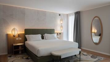 Camera d'albergo con un letto, comodini, una panca, uno specchio fissato alla parete e un tappeto decorato.