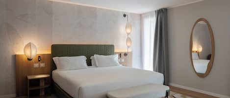 A hotel room with a bed, bedside tables, a bench, a wall-mounted mirror, and a patterned rug.