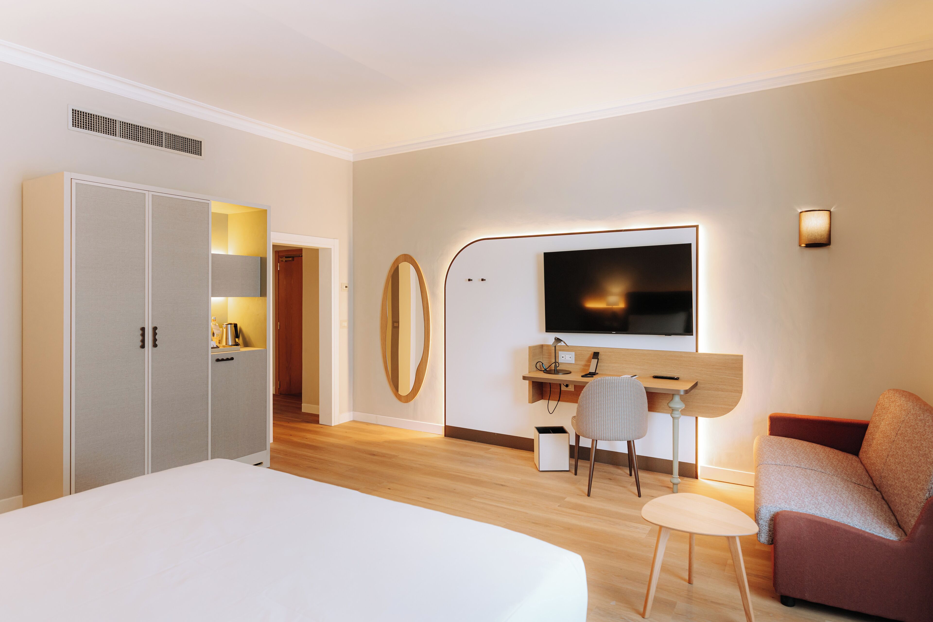 A modern hotel room with a large bed, a desk with a chair, a television, and a wardrobe.