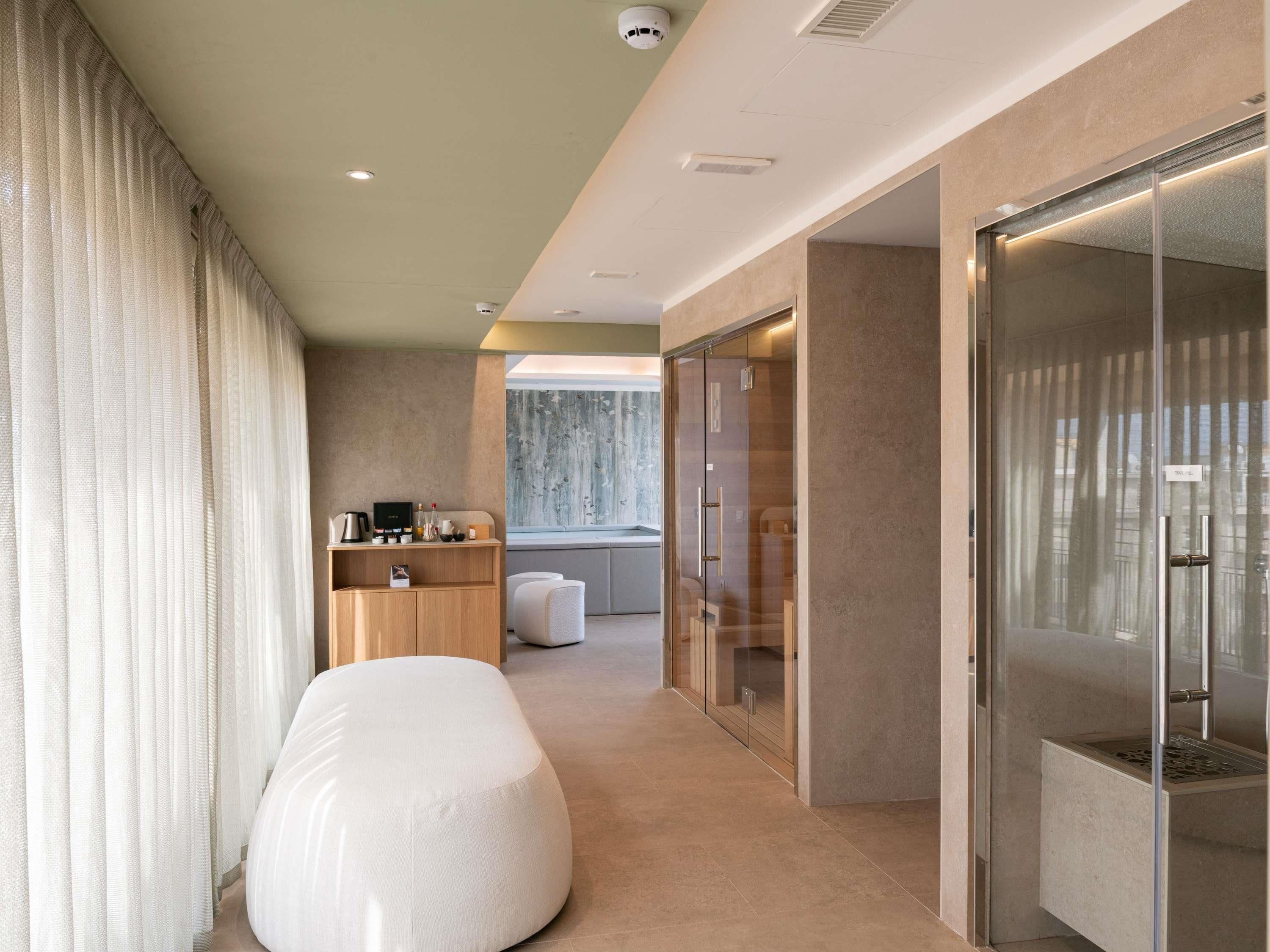 Ein modernes Hotelzimmer mit einem großen Bett, einer Sitzecke, einer Küchenzeile und einer gläsernen Dusche.