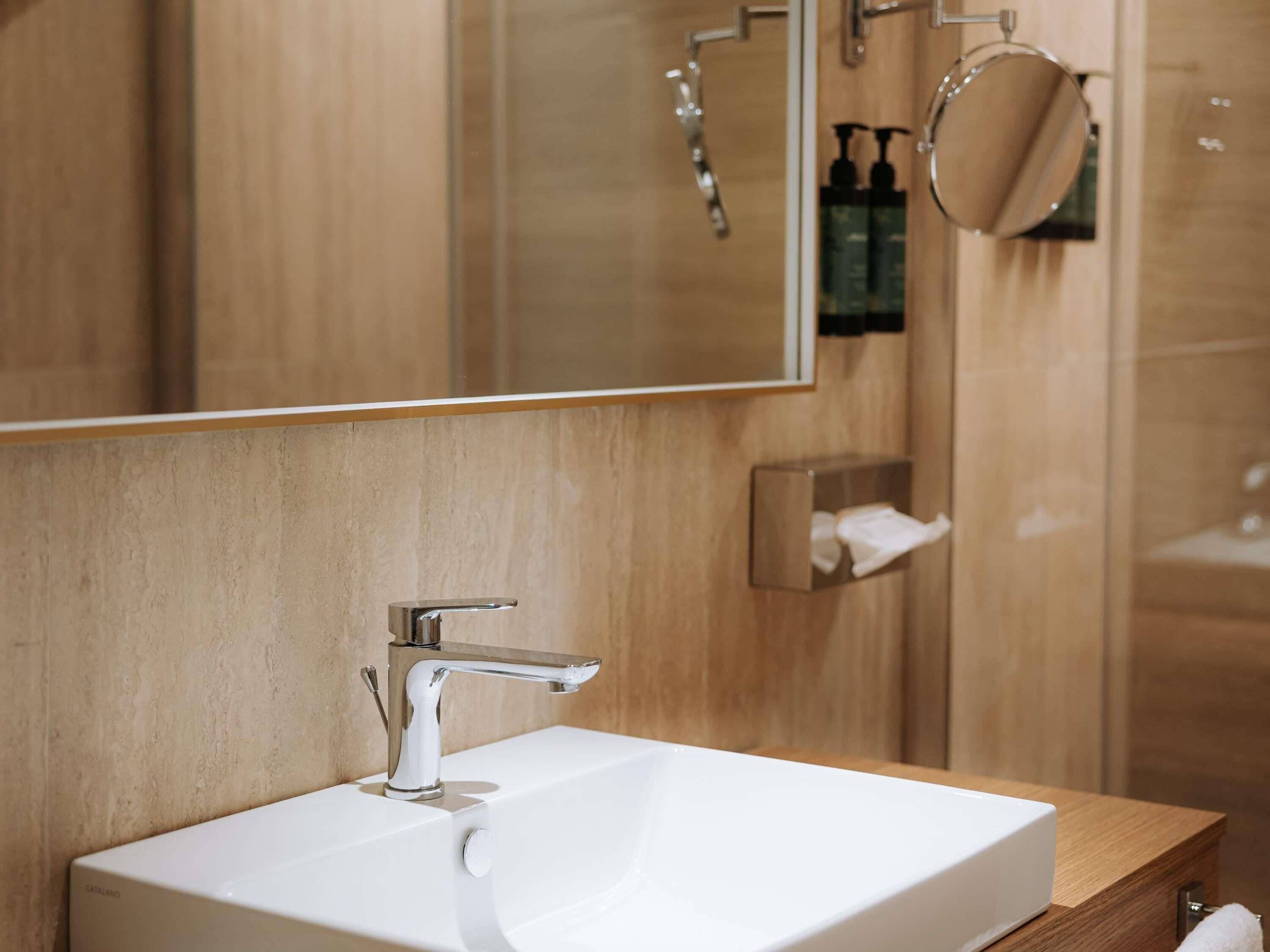 Un bagno moderno con un lavandino bianco, rubinetteria cromata e uno specchio grande.