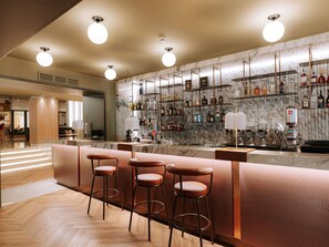 A bar area with a marble wall, multiple liquor bottles, and bar stools. - Mövenpick Hotel Bari (Bari)