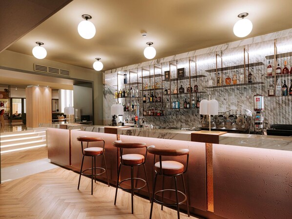 A bar area with a marble wall, multiple liquor bottles, and three bar stools. - Mövenpick Hotel Bari (Bari)