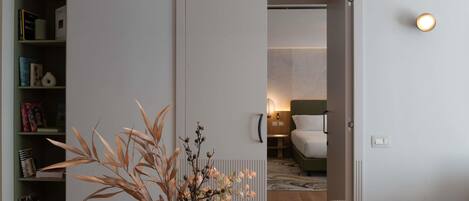 Una habitación de hotel moderna con comedor, cama con cabecera verde y lámpara fijada a la pared.
