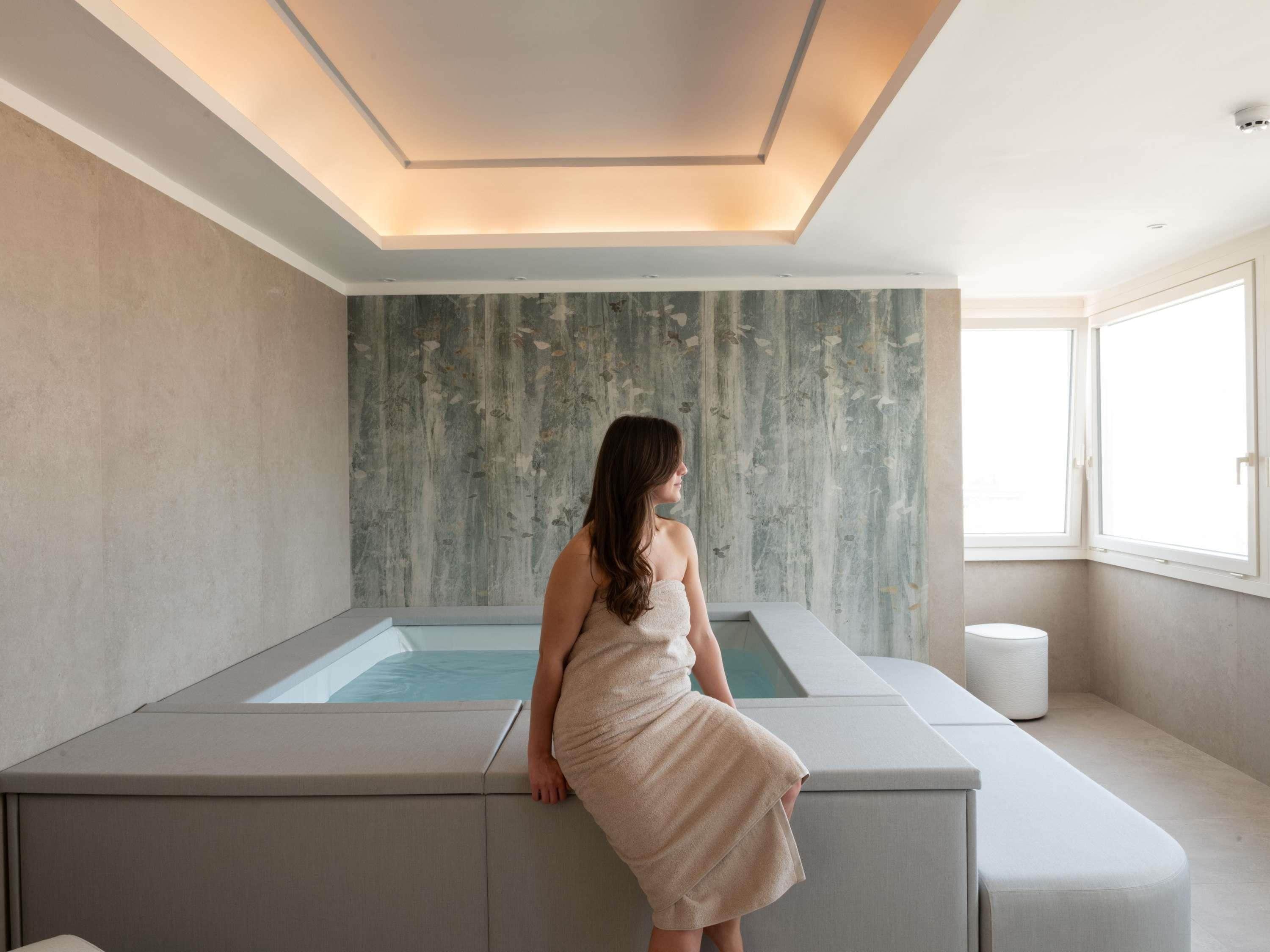 Une salle de spa dotée d’une grande baignoire, d’un banc et d’une fenêtre laissant entrer la lumière naturelle.