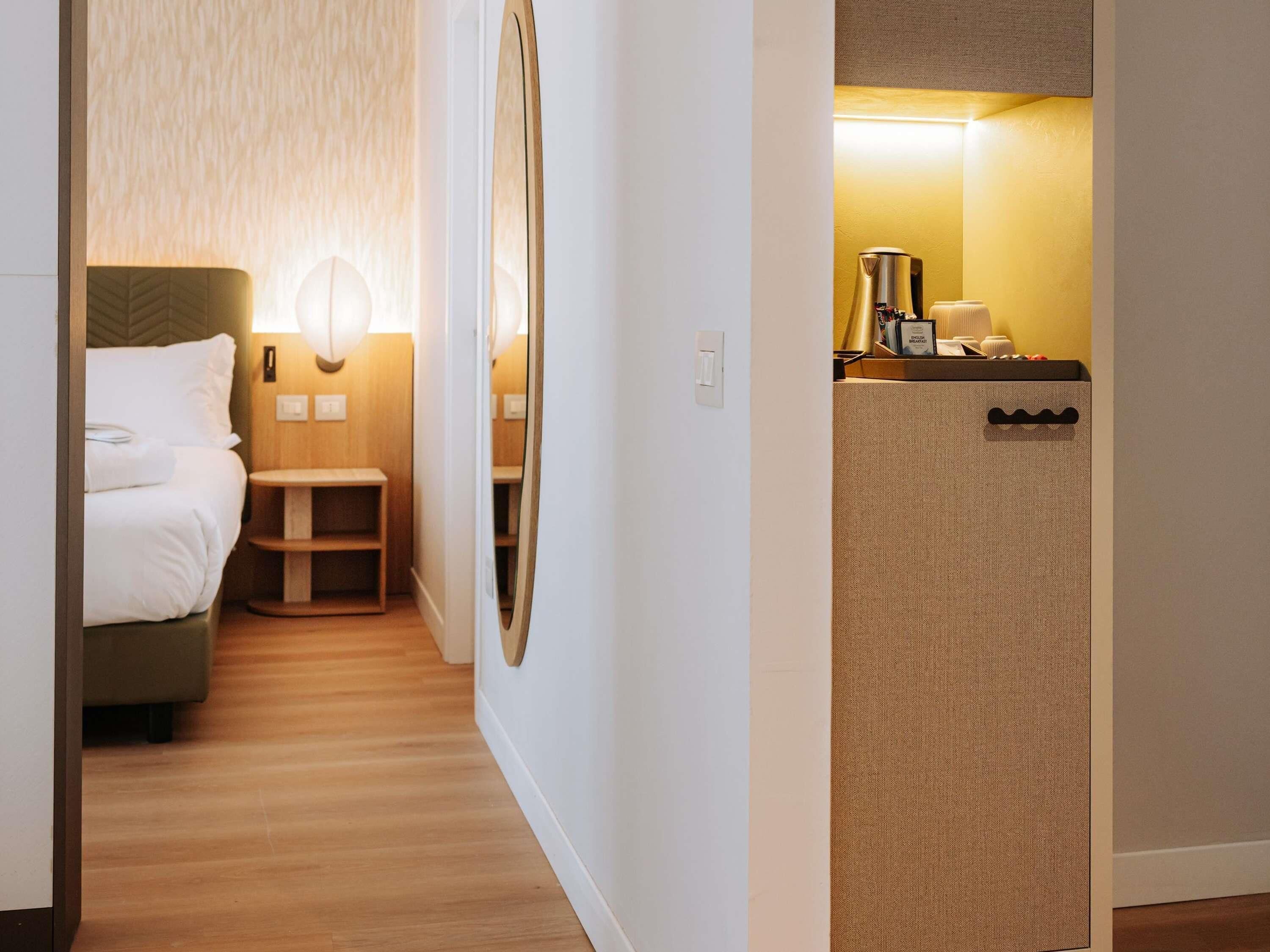A hotel room with a bed, bedside table, and a small seating area. There is a kitchenette with a coffee maker and a microwave.