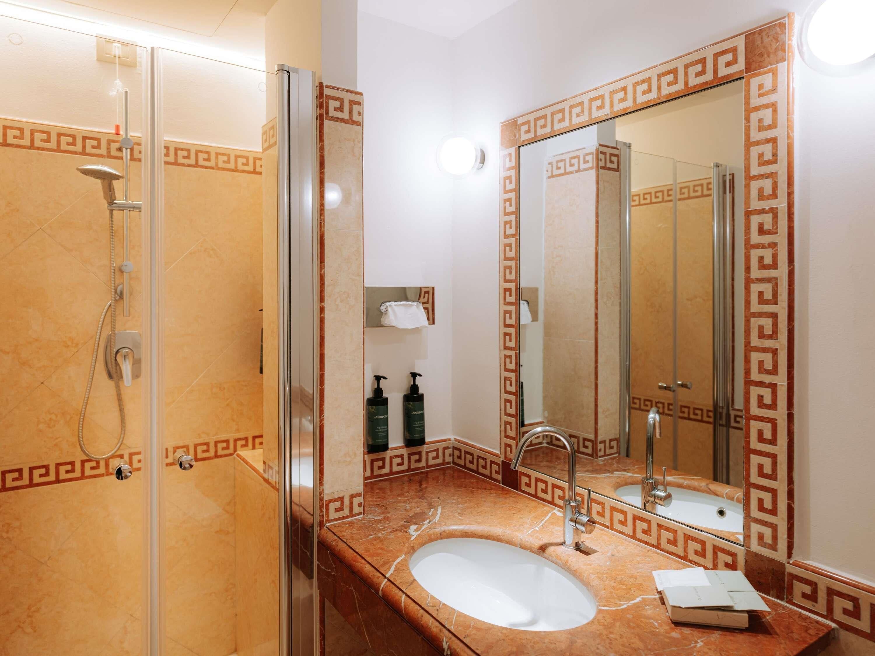 A bathroom with a glass-enclosed shower, a sink with a marble countertop, and a mirror with a decorative frame.