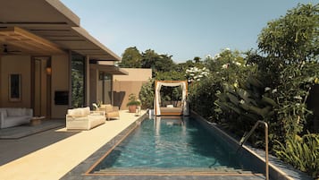 Un área de piscina moderna al aire libre con zona de estar, un espacio de relajación cubierto y abundante vegetación.