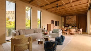 A modern living room with a large sectional sofa, a dining area with a table and chairs, and large windows offering a view of the outdoors.
