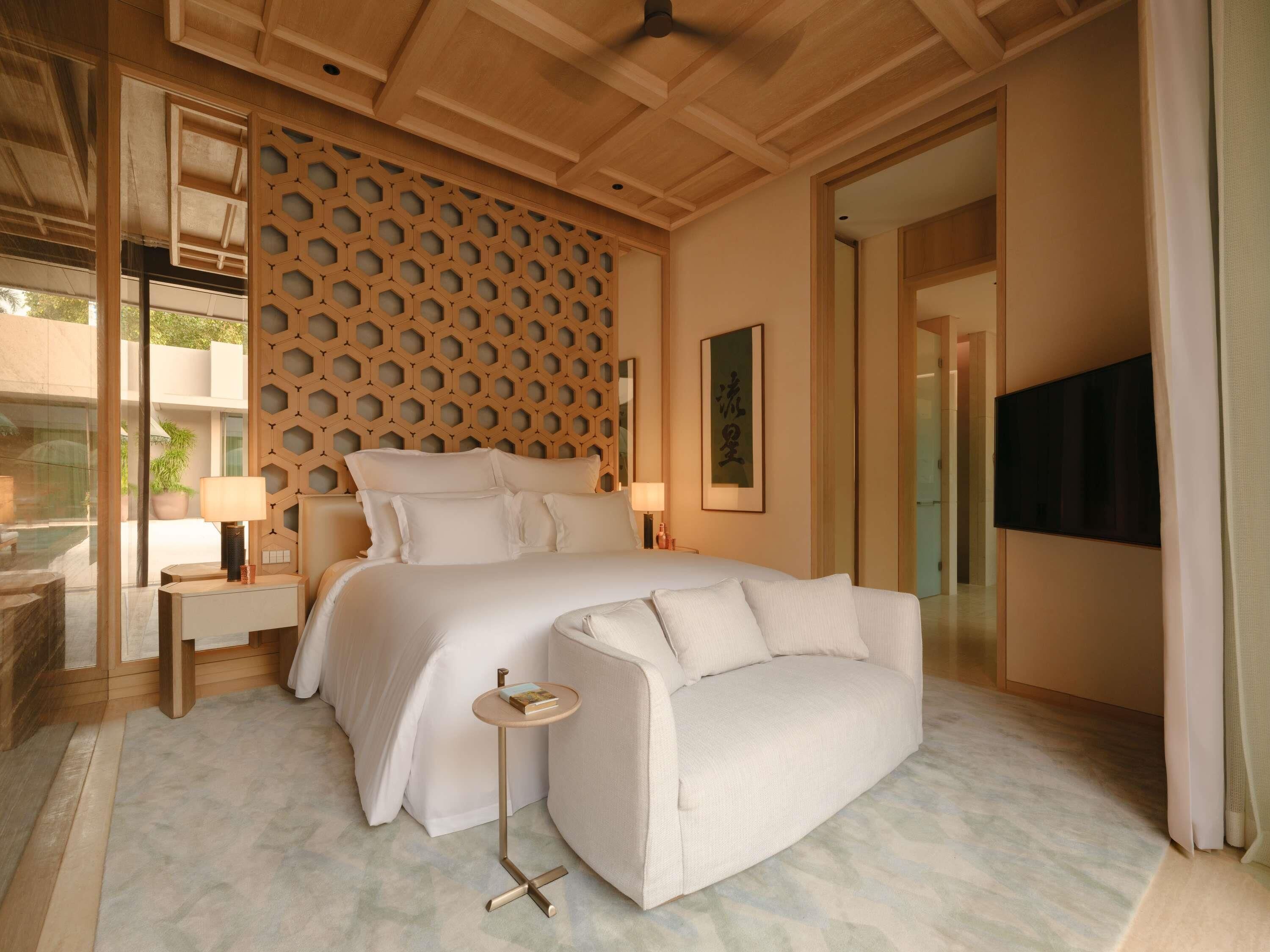 Een moderne slaapkamer met een groot bed, een nachtkastje met een lamp, een klein rond tafeltje en een televisie aan de muur.