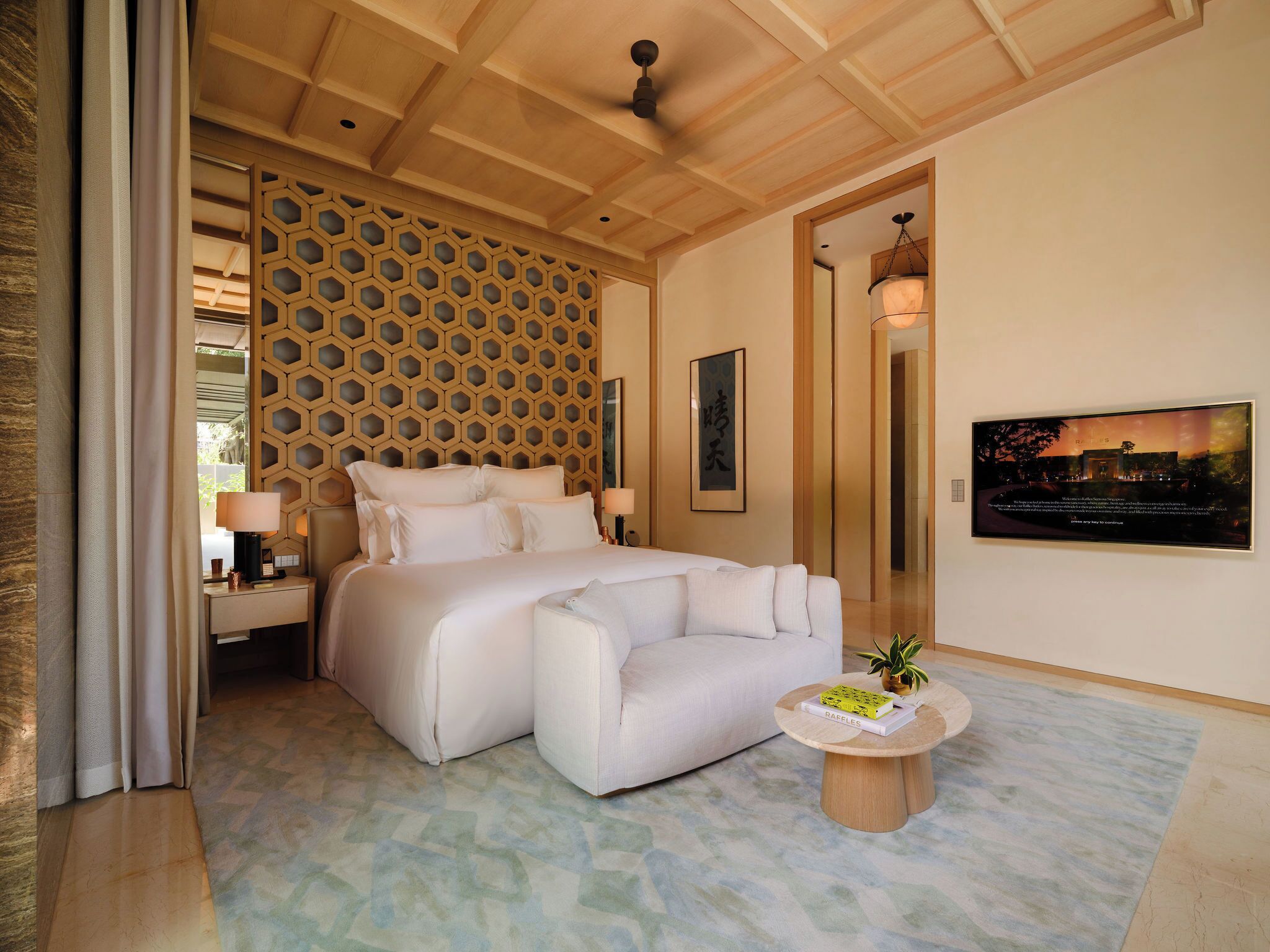 Une chambre moderne avec un grand lit, un canapé, une table ronde en bois et un téléviseur fixé au mur.