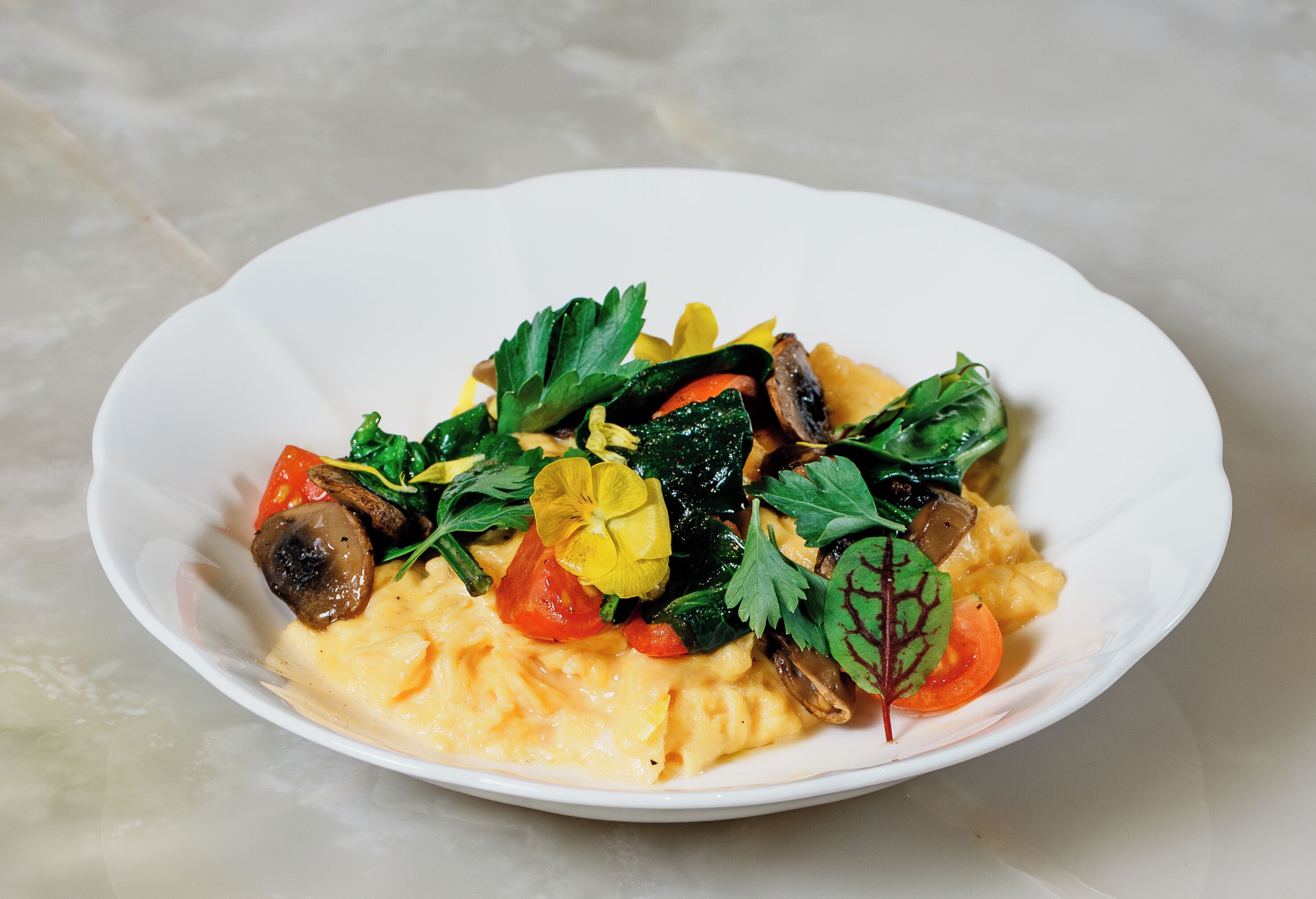 Une assiette blanche contenant des œufs brouillés, des champignons, des tomates et des légumes verts.