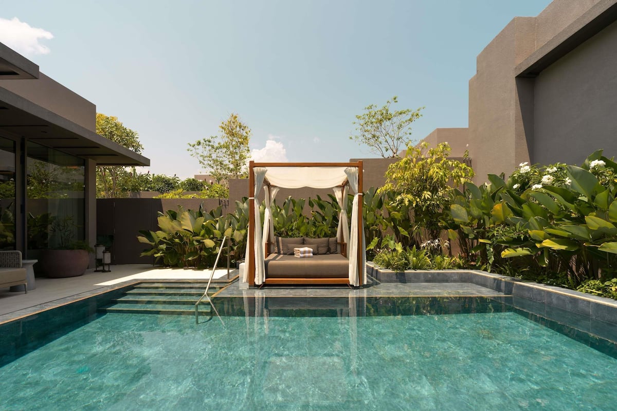 A clear swimming pool with a wooden canopy bed in the center.