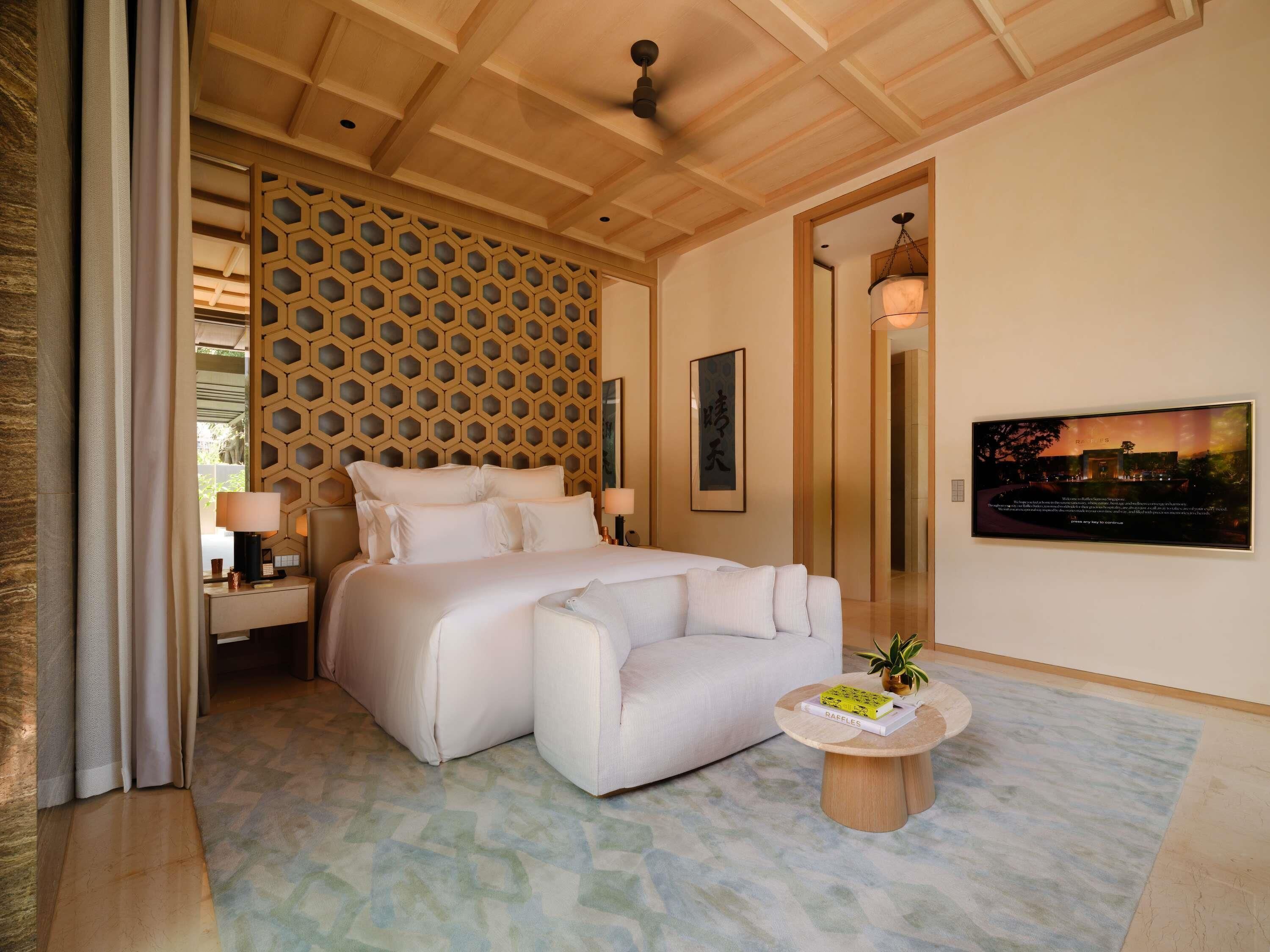 A hotel room with a large bed, a sofa, a round coffee table, a wall-mounted TV, and a decorative wooden panel.
