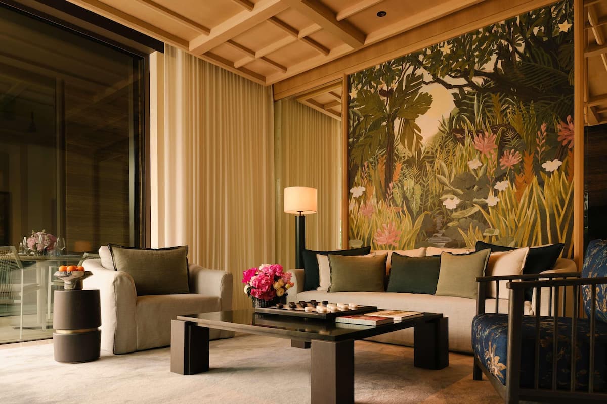 A modern living room with a glass coffee table, two sofas, and a large floral mural on the wall.
