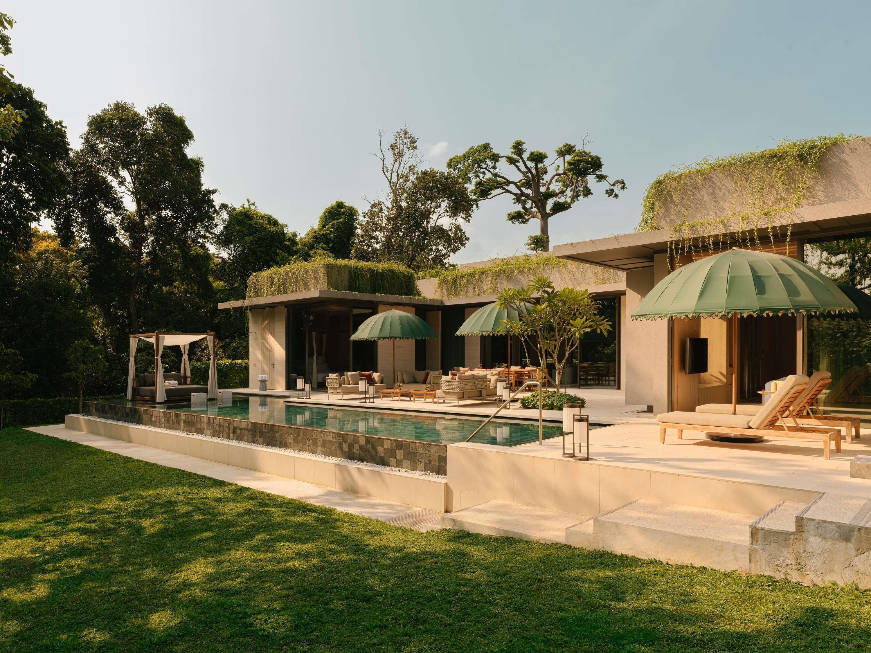 A modern outdoor pool area with lounge chairs and umbrellas, surrounded by lush greenery and a well-maintained lawn.