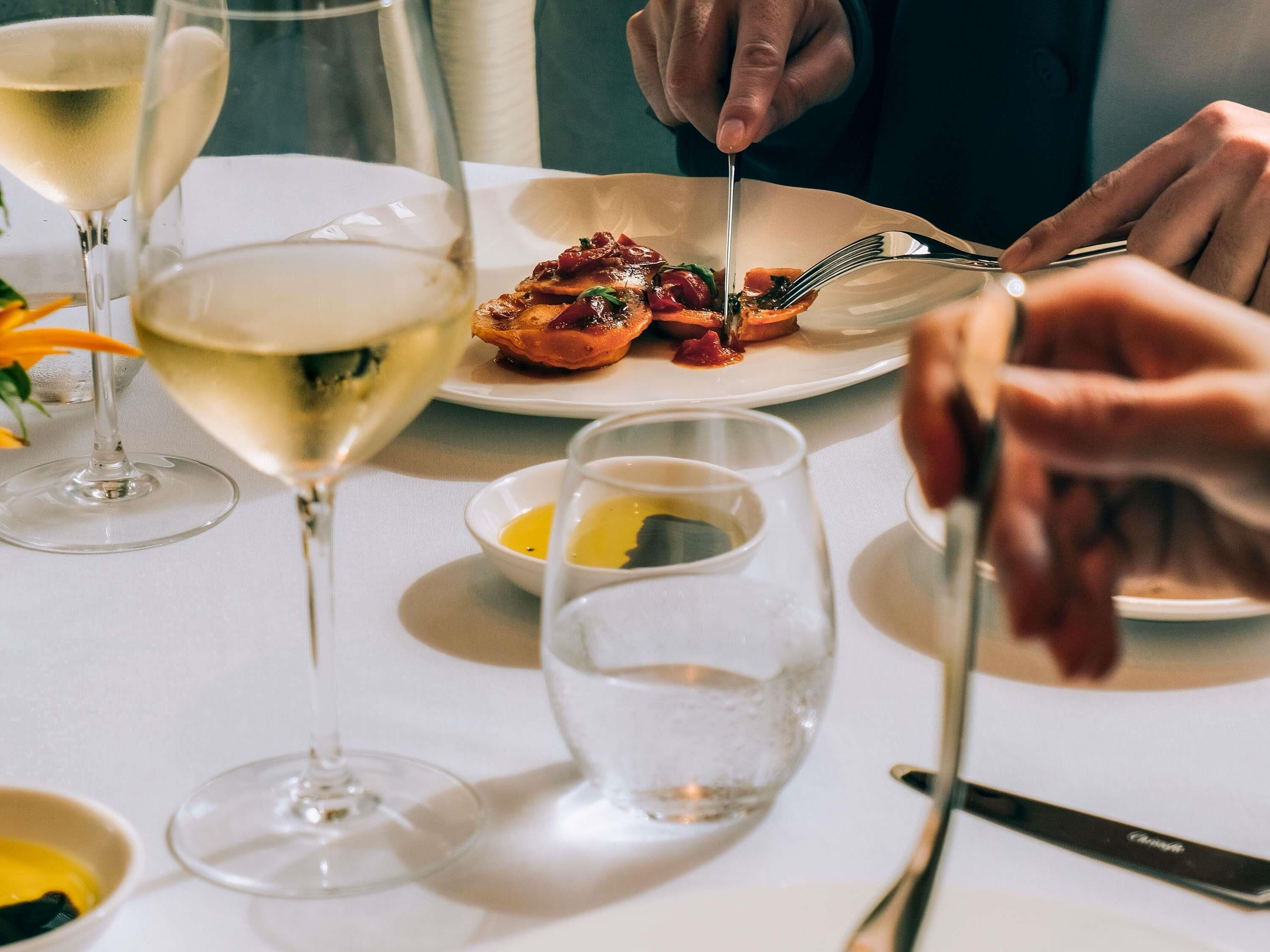 A dining table with a plate of food, glasses of white wine, and a knife.