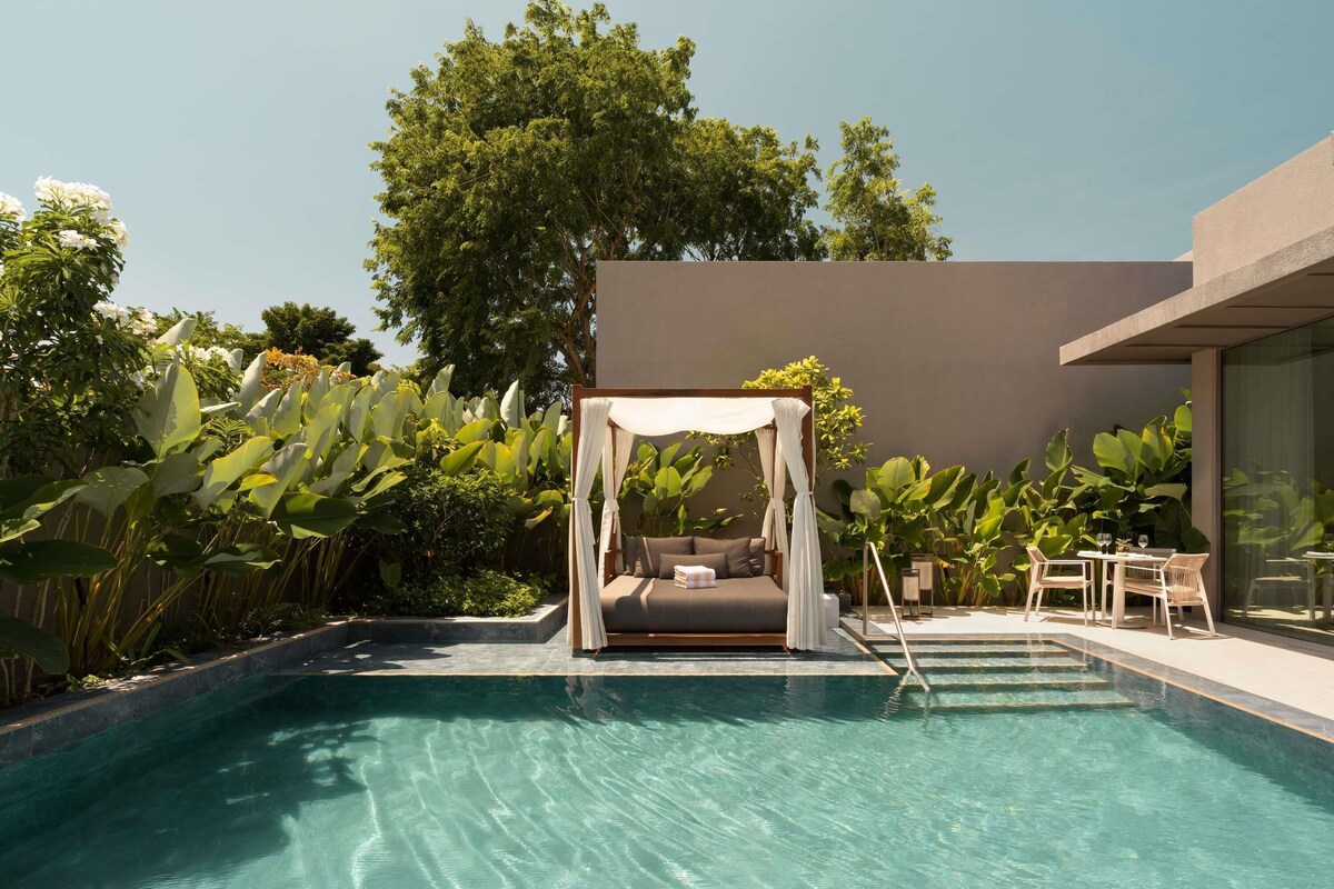 A pool with a canopy bed, surrounded by lush greenery and modern architecture.