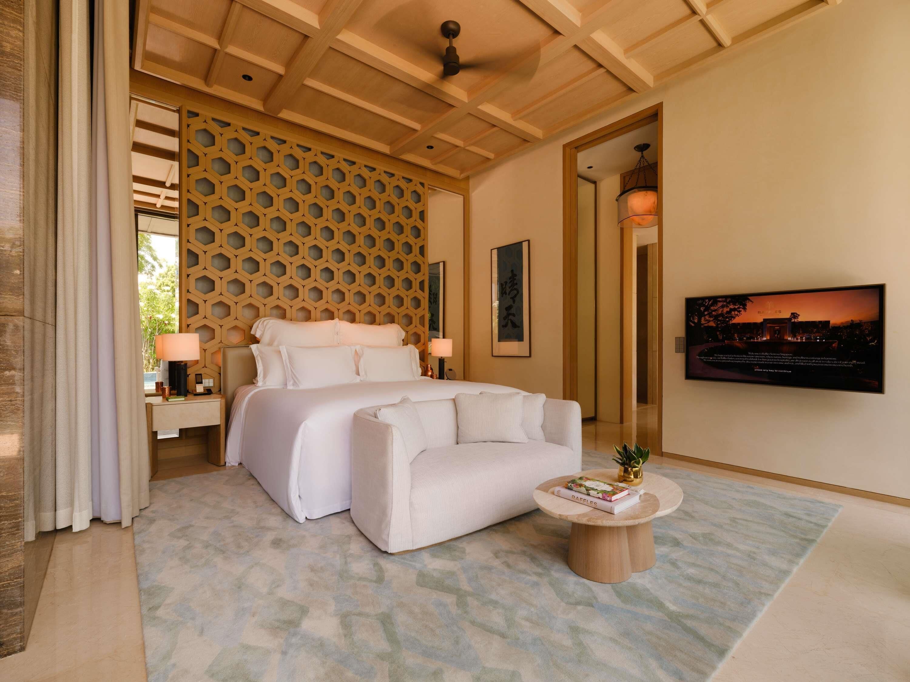 A bedroom with a bed, bedside tables, a sofa, a coffee table, a wall-mounted TV, and a decorative wall panel.