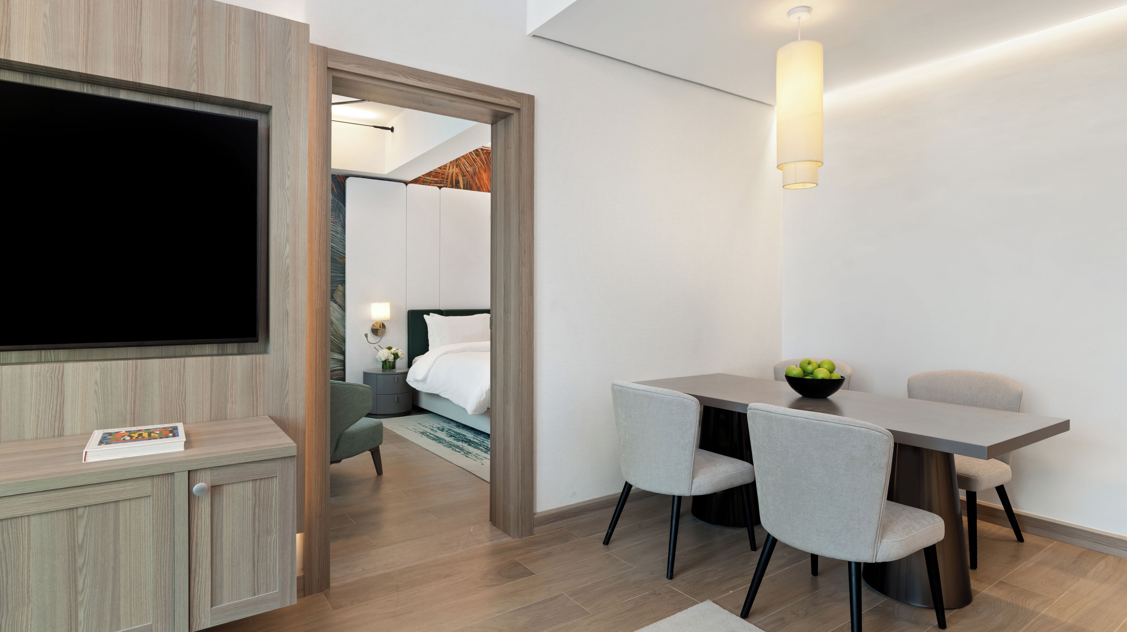 Una camera d'albergo moderna con televisione a schermo piatto, un tavolo da pranzo con sedie, un piccolo tavolino e un letto con testiera.