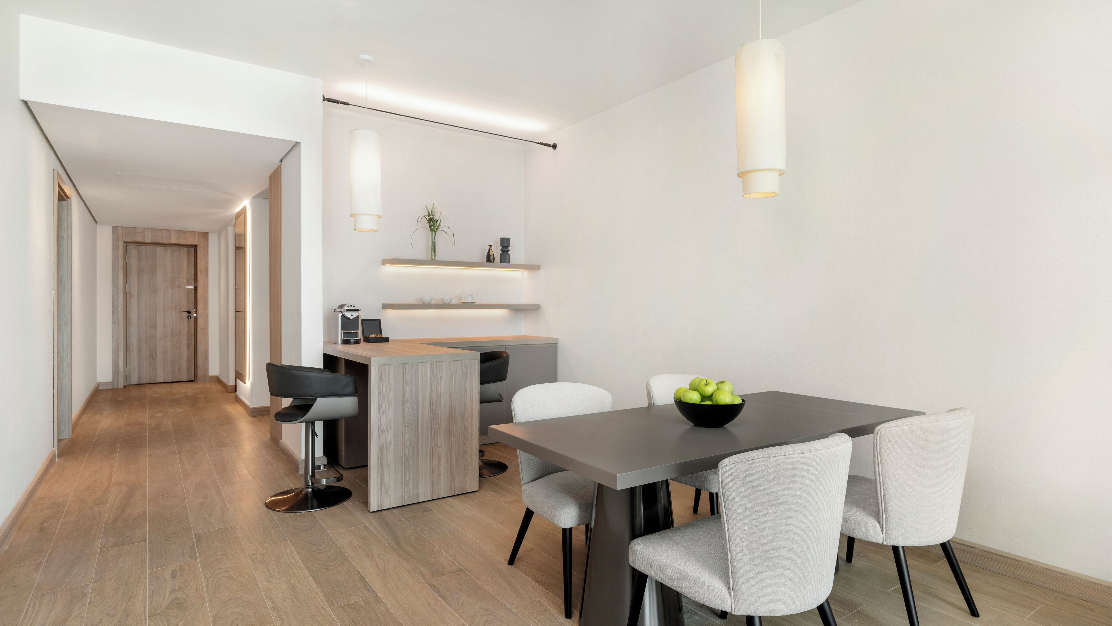 Uma cozinha moderna com uma ilha central, uma área de jantar com mesa escura e cadeiras cinzas, e um corredor que dá para outro espaço.