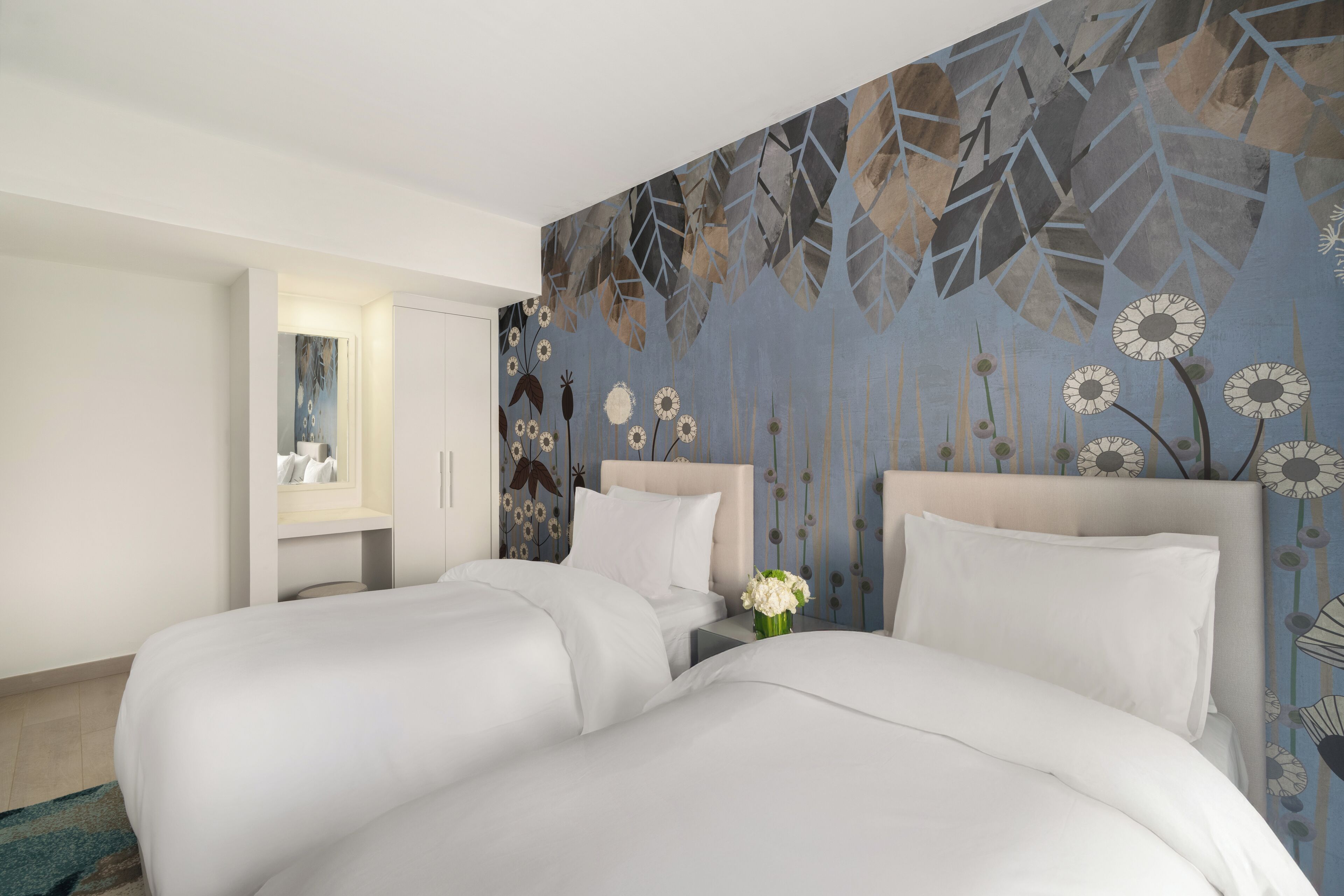 Une chambre d’hôtel avec deux lits, une table de chevet, un miroir et un mur décoratif.