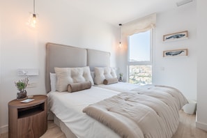 Quarto com cama grande, mesa de cabeceira e janela com vista para a paisagem urbana.