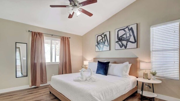 Ein Schlafzimmer mit einem großen Bett, einem Deckenventilator, Kunstwerken an der Wand und einem Fenster mit Jalousien.