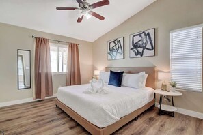 Ein Schlafzimmer mit einem großen Bett, einem Deckenventilator, Kunstwerken an der Wand und einem Fenster mit Jalousien.