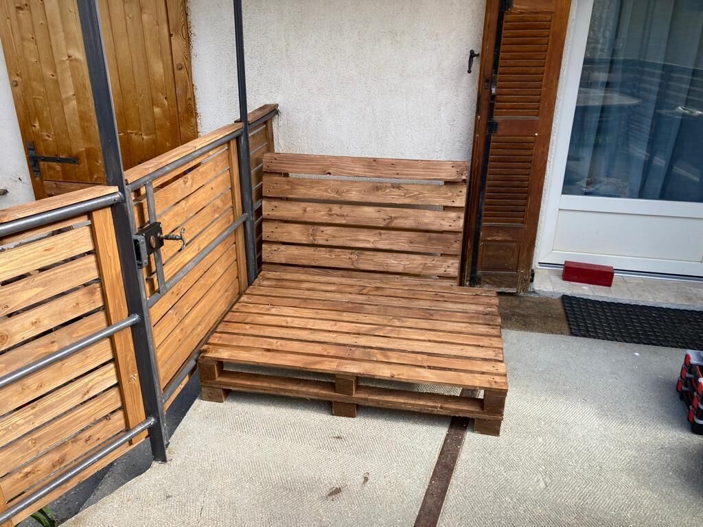 Un banc en bois avec des garde-corps en métal, un sol en béton et une porte dotée d’une vitre.