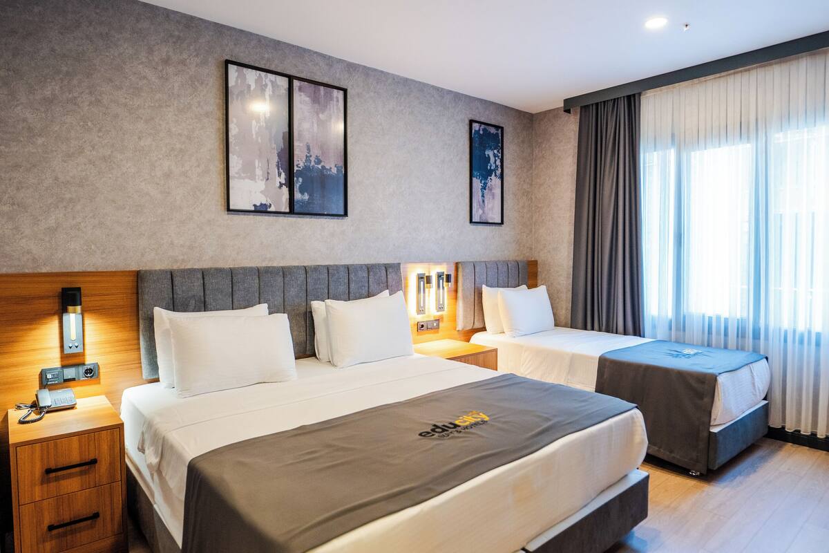 A modern hotel room with a large bed, bedside tables, a desk, and a window with curtains.