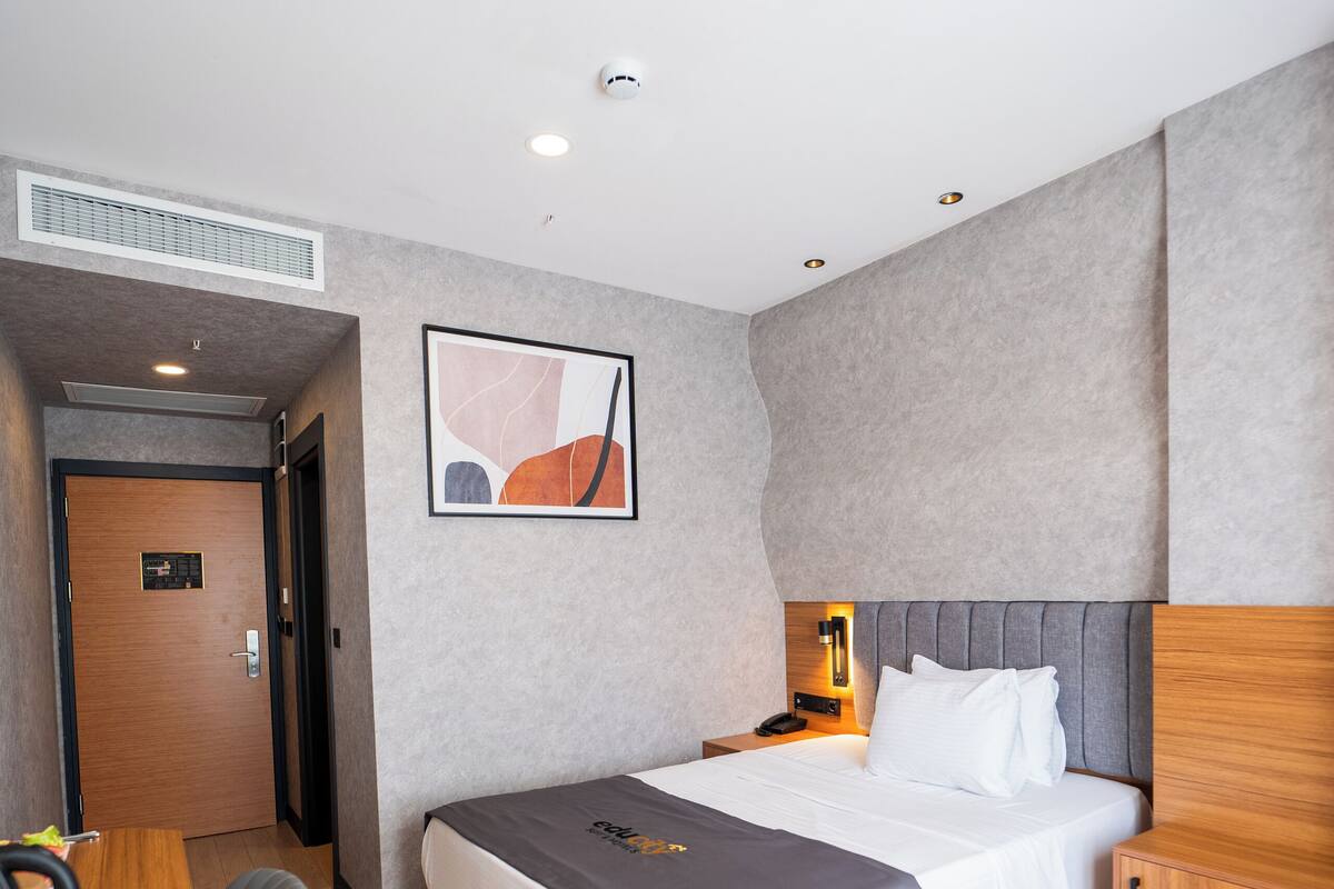 A modern hotel room with a bed, bedside table, and a desk.