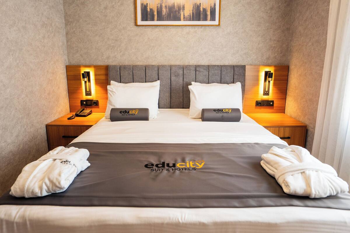 A hotel room with a large bed, two bedside tables, a headboard, and a framed picture on the wall.