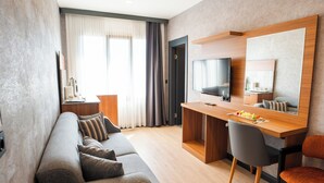Una moderna camera d'albergo con divano, scrivania, televisione e un ampio specchio.