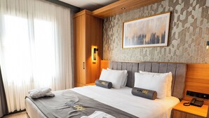 Una camera d'albergo moderna con un ampio letto, una testiera in legno e un quadro raffigurante un panorama urbano.