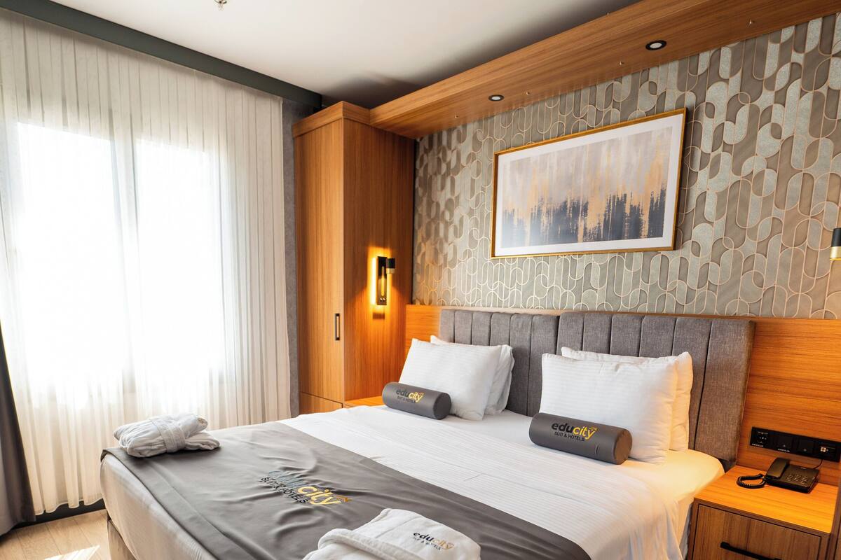 A modern hotel room with a large bed, wooden headboard, and a cityscape painting on the wall.