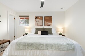 A bedroom with a large bed, two bedside lamps, a bench, and abstract wall art.