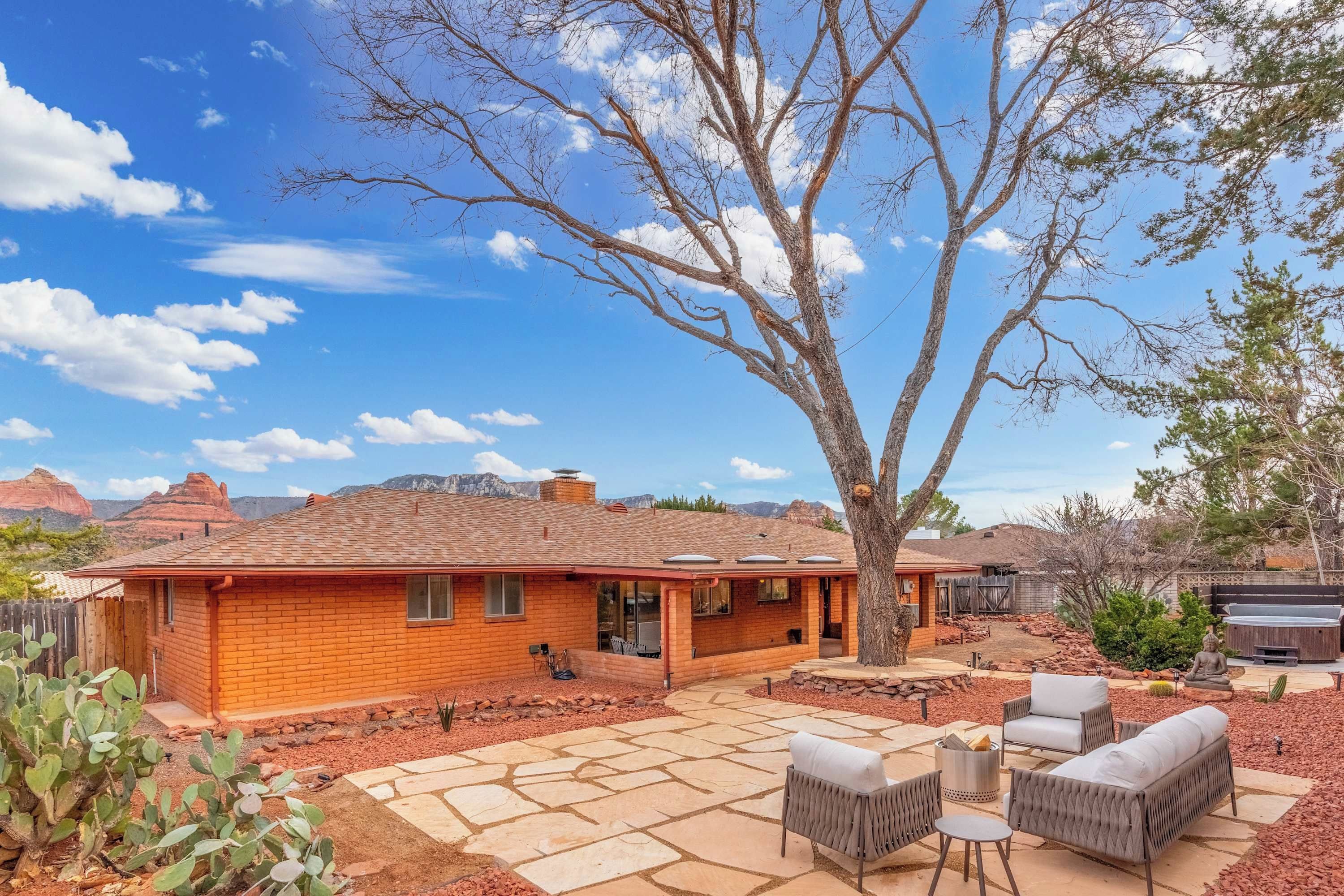 A single-story brick house with a patio area, outdoor furniture, and a large tree.