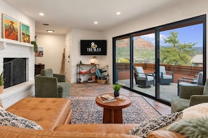 A spacious living room with a fireplace, comfortable seating, a coffee table, and a large window offering a view of the outdoors.