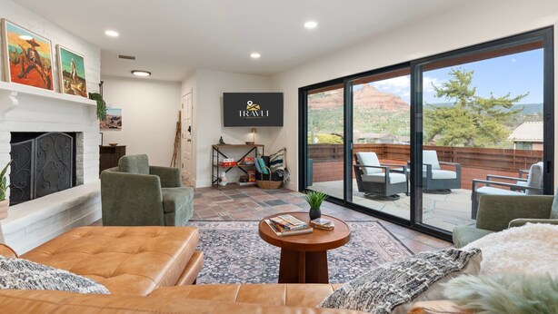 A modern living room with a fireplace, comfortable seating, a flat-screen TV, and a large sliding glass door leading to an outdoor patio. - Uptown Red Rock Retreat | Hot Tub & Patio Views (Sedona)