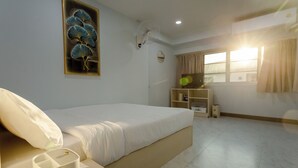 A bedroom with a bed, bedside table, lamp, and a wall-mounted fan. - Rama Residency Sukhumvit Bangkok (Bangkok)