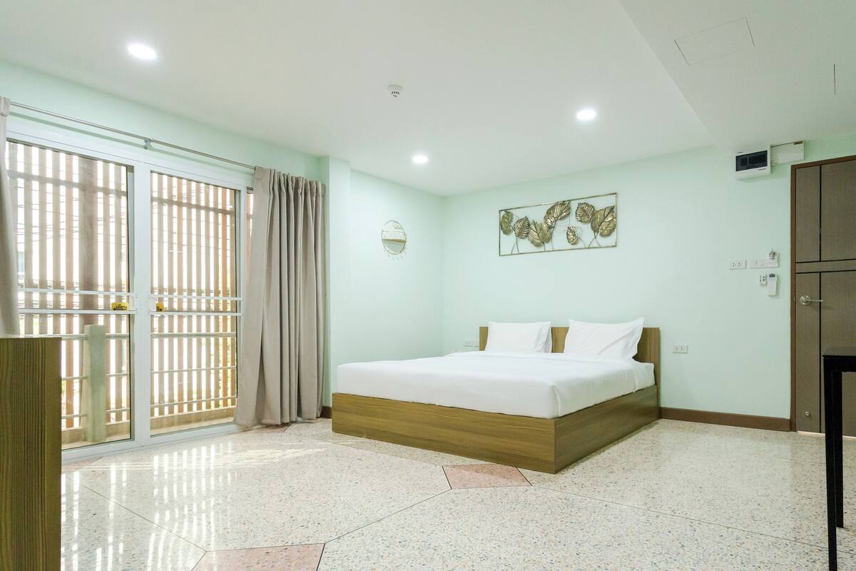 A bedroom with a bed, a window with blinds, a wall-mounted artwork, and a door.