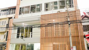 A multi-story building with a modern design, featuring a staircase leading to the entrance, a small outdoor seating area with a table and chairs, and a visible balcony on the upper floor. - Rama Residency Sukhumvit Bangkok (Bangkok)