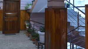 Un corridoio con pavimento in marmo, una porta in legno, una scala dal design particolare e piante in vaso lungo la parete.
