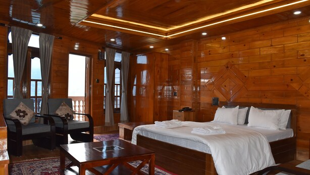 Una camera in legno con un letto, una poltrona, un tavolo e una finestra con tende.