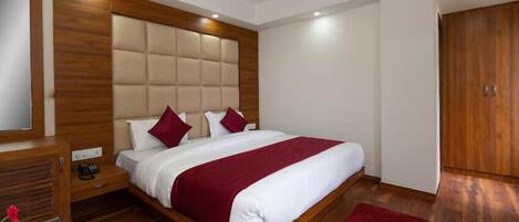 A modern bedroom with a wooden headboard, a large bed with red and white bedding, a nightstand, a wooden wardrobe, and a red rug.