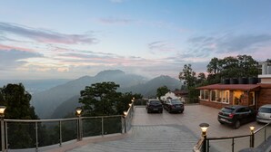 Un hotel con vista a las montañas, un estacionamiento con autos y un edificio de madera con techo rojo.