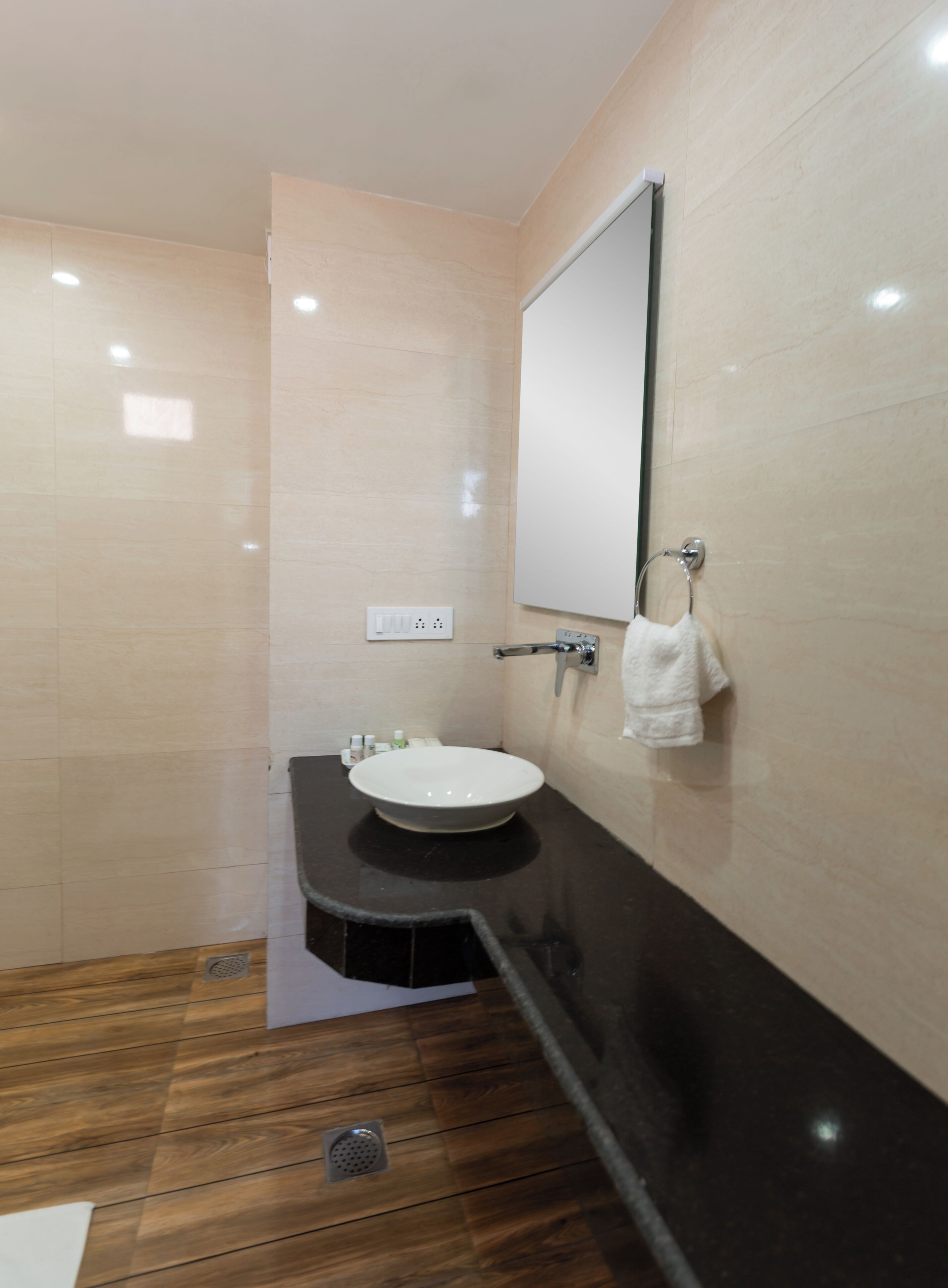 A bathroom with a sink, mirror, towel rack, and wooden flooring.