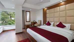 Un hotel moderno con una cama grande, ventilador de techo, cabecero de madera y vista a los árboles por la ventana.