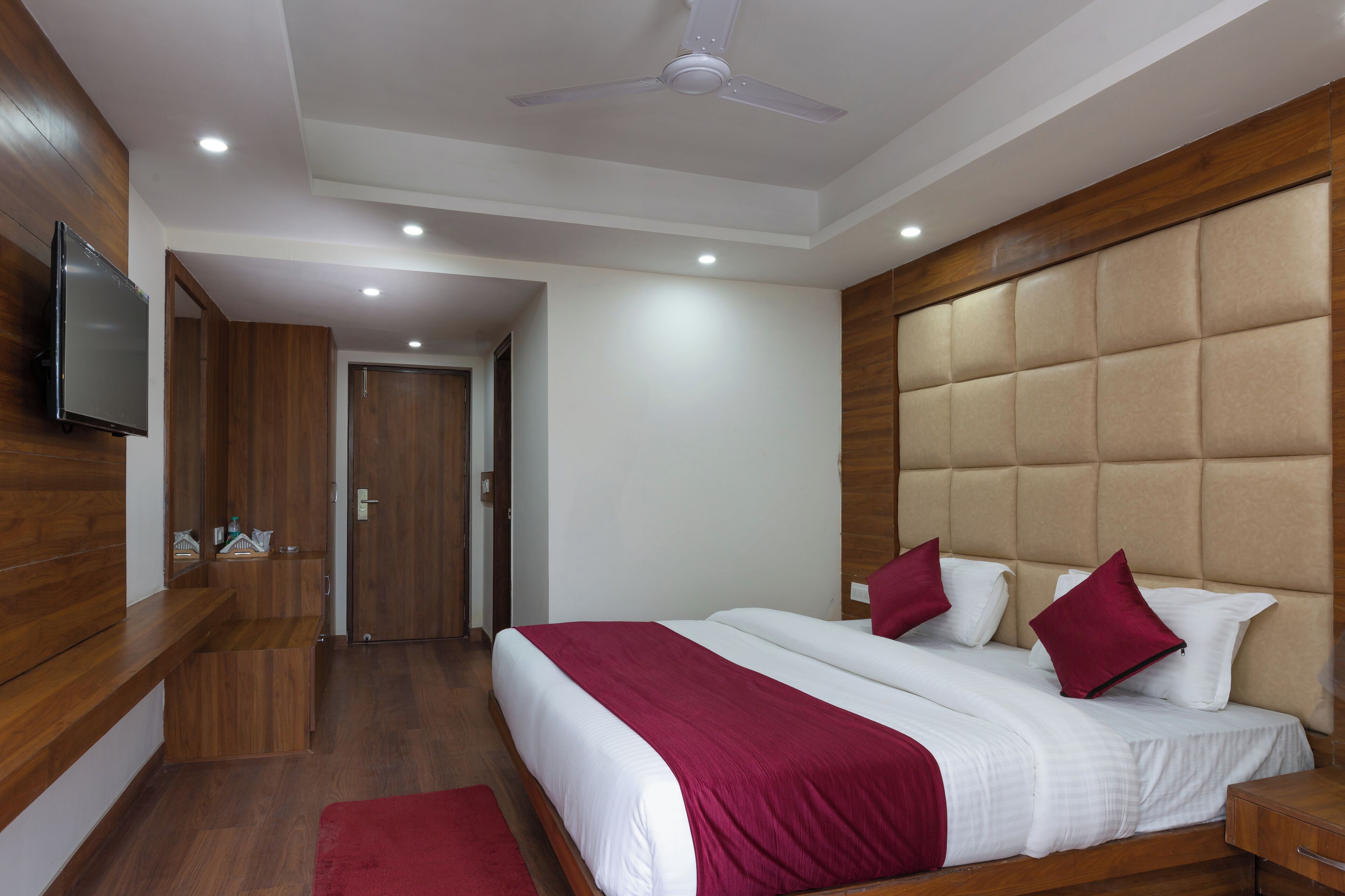 A hotel room with a bed, a TV, a ceiling fan, and wooden paneling.
